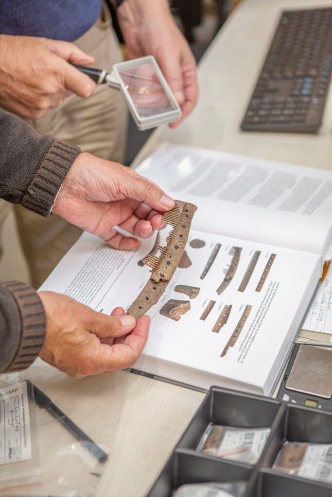 Man houdt houten kam vast om te vergelijken met een afbeelding uit een boek.