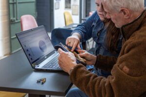Jonge vrouw helpt oudere man met het identificeren van een fysiek object met behulp van een laptop
