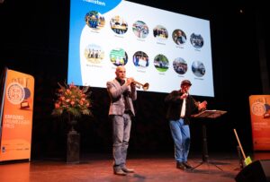 Op een podium staat een man met een trompet en een man met een microfoon