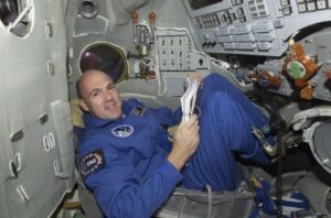 Astronaut André Kuiper in gehurkte horizontale houding in een ruimtevaartschip