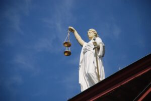 Een beeld van vrouwe justitia van onderaf, tegen een blauwe hemel